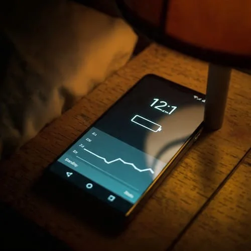 Android phone battery dropping overnight showing standby drain on a bedside table